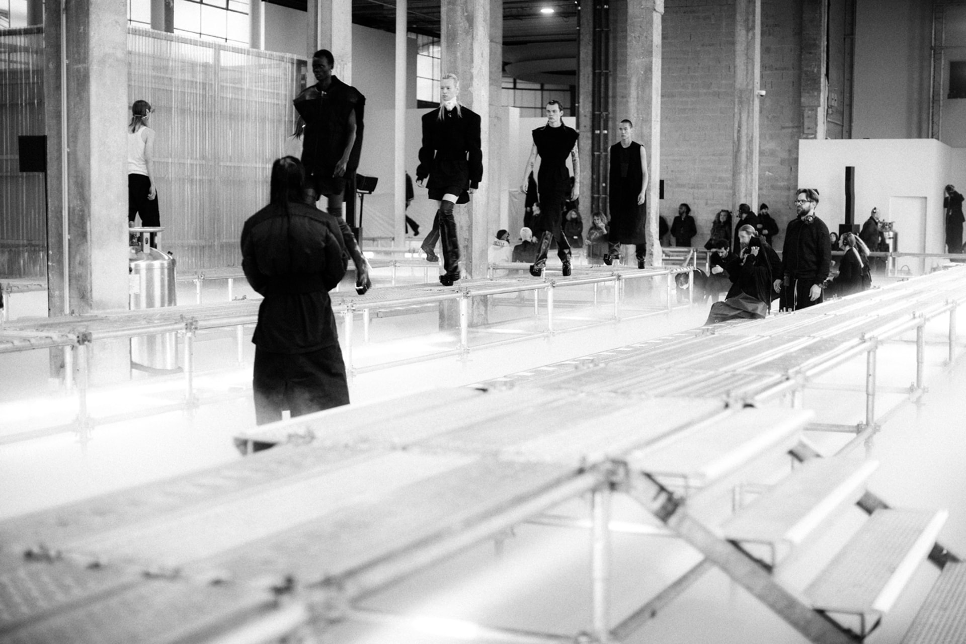 Models in dark, architectural tailoring walk a fog-lit scaffolding runway